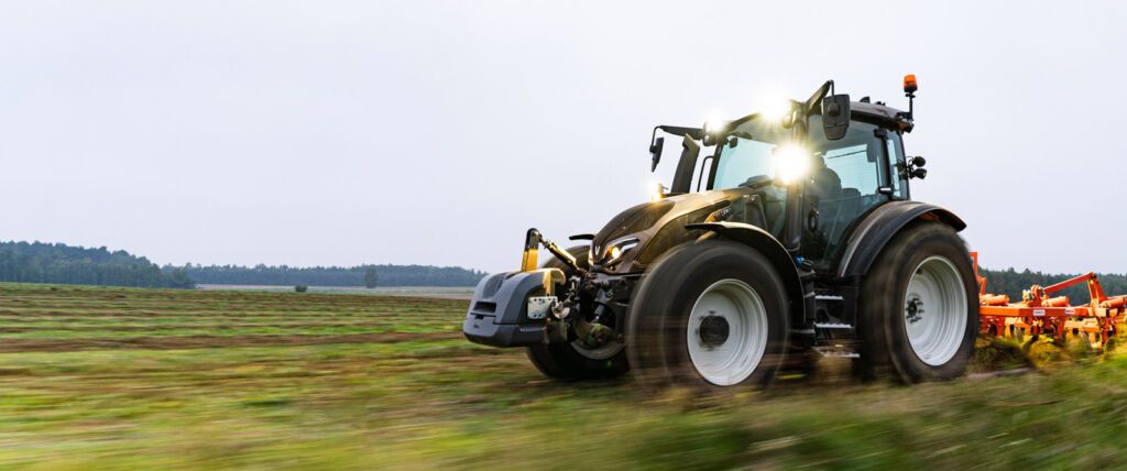 Valtra G135 traktor med frontlaster parkert på gårdsplass. Moderne design i rød og svart, kjent som Norgestraktoren for sin kompakte størrelse og 145 hk motor. En allsidig traktor ideell til frontlasterarbeid, med god sikt og avanserte Smart Farming-funksjoner.